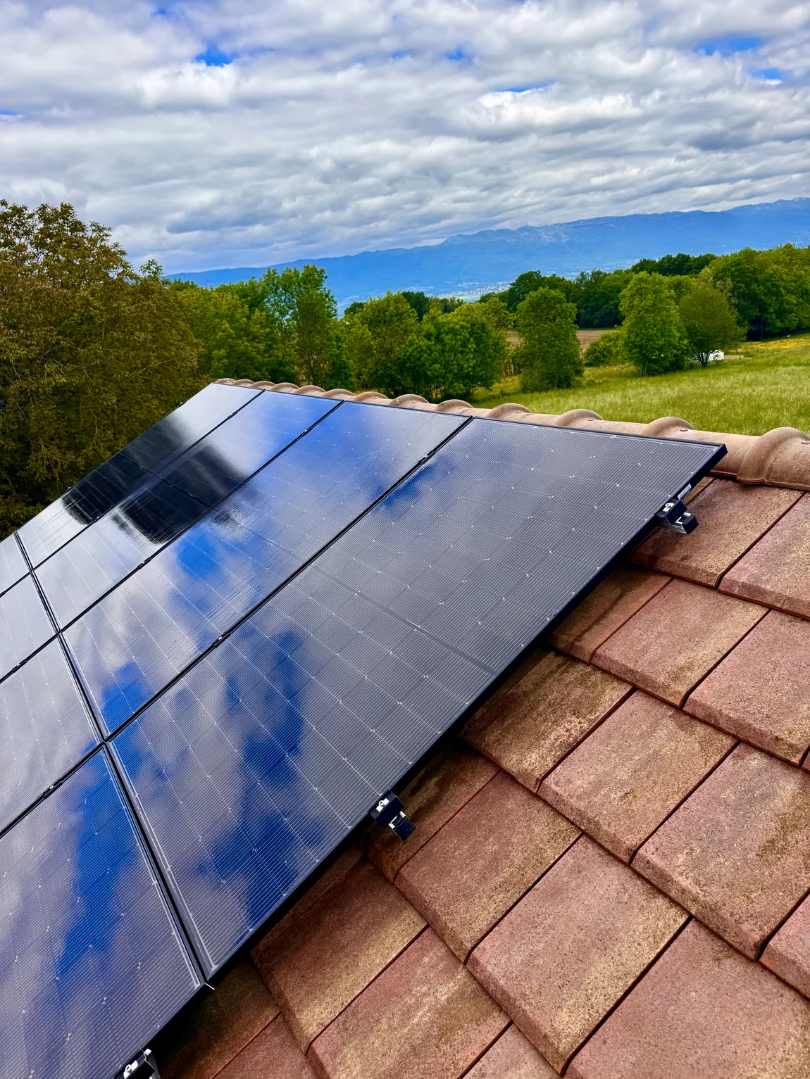 Panneaux photovoltaïques propres sur un toit en tuiles, vue dégagée sur la campagne et les montagnes du Léman
